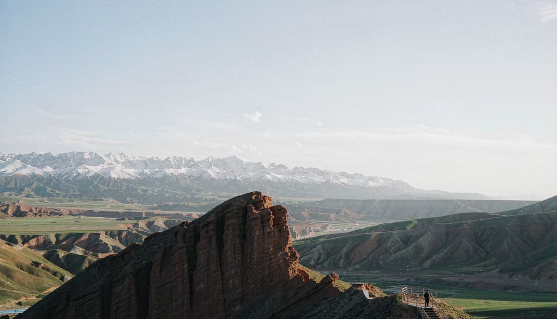 Mirador sobre un mosaico de valles verdes y ocres con picos nevados al fondo