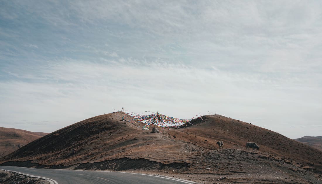 Paso de montaña con banderas de oración tibetanas y la carretera subiendo hacia el collado
