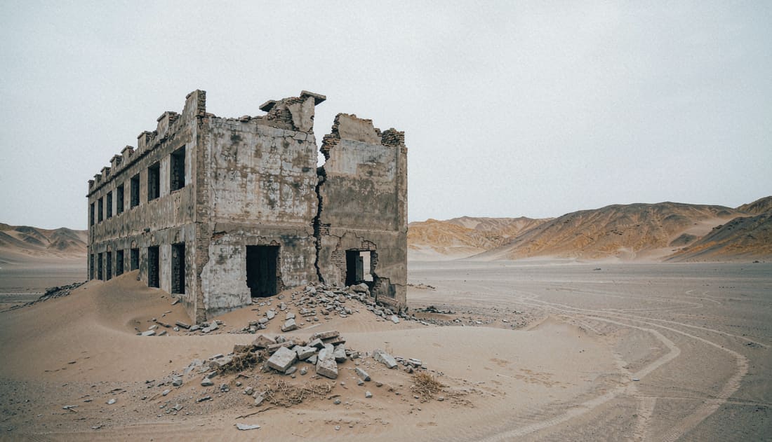 Edificio de hormigón abandonado semienterrado en la arena, con ventanas vacías